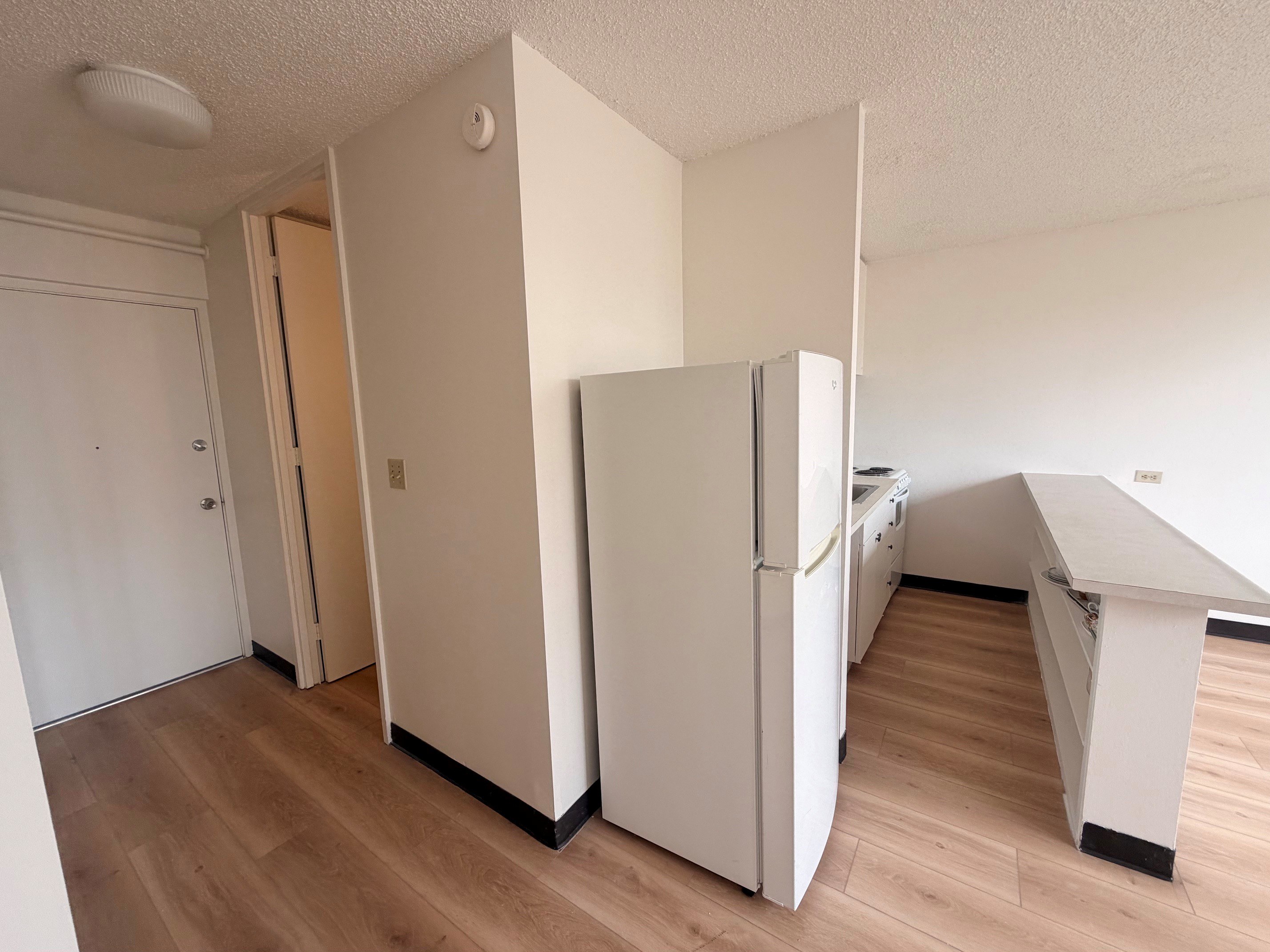 A white refrigerator is in the corner of a room with wood flooring.